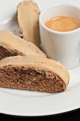 Top view, close up of three, freshly baked coffee, chocolate, chunky, biscotti with caramel glaze on round, white plate and a cup of espresso