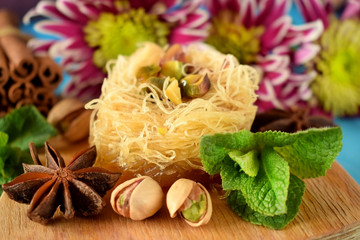 Fototapeta na wymiar Egyptian dessert Kunafa made of kataifi dough with pistachios surrounded by spices, flowers and nuts