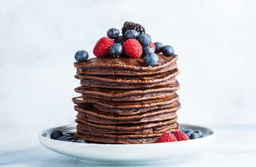 Flowing maple syrup on a pile of chocolate pancake with fresh berries. morning healthy breakfast