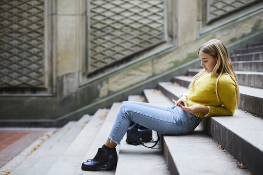 Young woman using smartphone while sitting on steps outdoors