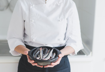 Little fishes in ceramic bowl over chef's hands.