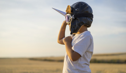 Little boy wearing helmet and dreams of becoming an aviator while playing a paper plane at sunset © Outsiderzone