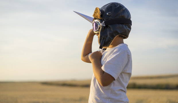 Little boy wearing helmet and dreams of becoming an aviator while playing a paper plane at sunset