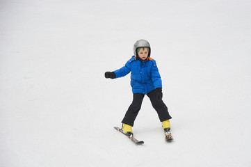 Fototapeta na wymiar Child boy skiing in winter mountains. Active kid with safety helmet and goggles. Ski race for young children. Winter sport for family. Kids ski lesson in school. Young skier racing in snow