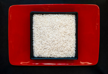 Rice Grains in Black Plate on Red Plate Background Surface