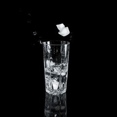 A glass of water with ice splash and spray. On a black background.