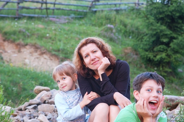 Fototapeta na wymiar Children with funny faces and a woman, their mom resting on a picnic in the mountains in the summer