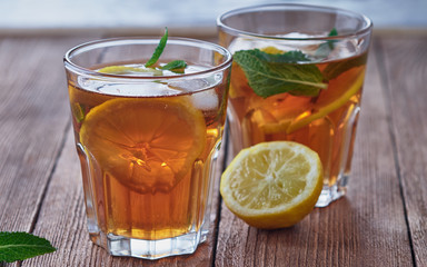 Ice tea with lemon and mint in a glass on a woodenbackground