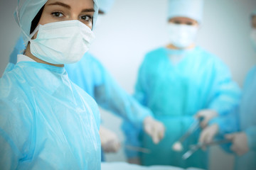 Medical team in masks performing operation. Focus on female doctor or intern girl. Medicine, emergency help concepts