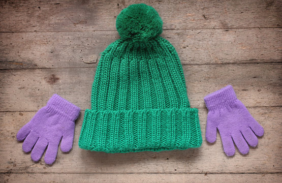 Children's winter accessories: hat and gloves. Rustic wooden background. Pastel green and purple colors.
