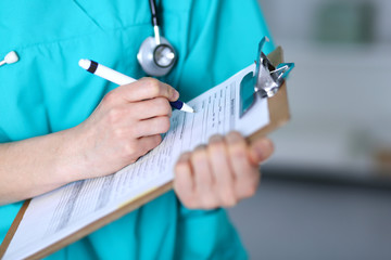 Female doctor filling up medical form on clipboard closeup.  Physician finish up examining his patient in hospital and ready to give a prescription to help. Healthcare, insurance and medicine concept 