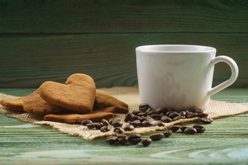 White porcelain cup, scattered coffee beans, homemade cookies on a wooden table