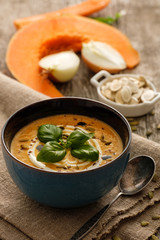 Delicious homemade pumpkin soup with basil leaves on rustic wooden table.
