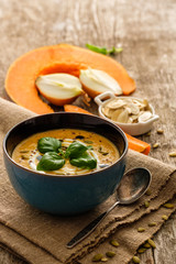 Delicious homemade pumpkin soup with basil leaves on rustic wooden table.