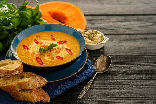 Delicious homemade pumpkin soup with prawns, chili and basil leaves on the wooden background. Copyspace.