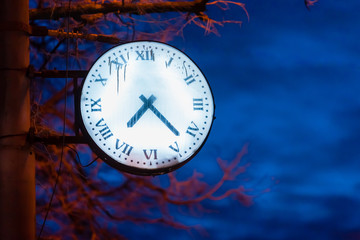 A clock with a glowing dial on a street lamppost at dusk