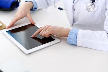Woman doctor using tablet computer while sitting at the desk in hospital closeup. Cardiologist checks heart diagrams with tablet pc. Healthcare, insurance and smart technology in medicine concept