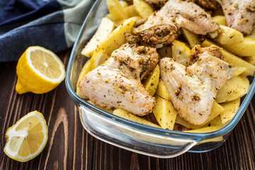 Raw chicken wings with potatoes marinated on a wooden background