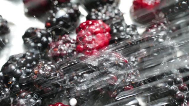 Close slow motion video of ripe blackberries being rinsed with water in a stainless steel colander.