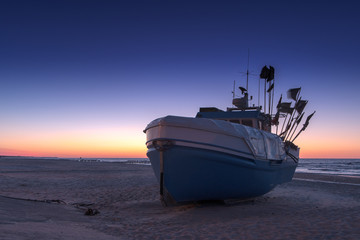 A fishing boat is lying on the beach during the blue hour. Concept: vacation and travel or boats