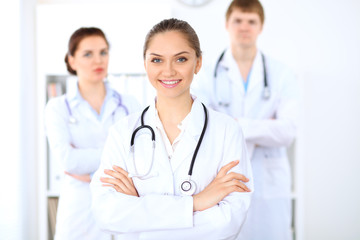 Fototapeta premium Happy female doctor keeping medical clipboard while medical staff are at the background