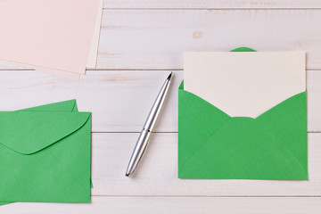 Top View of a invitation or Letter with a Green Envelope. Message or Ticket on Wooden White Desk or Table. Writing a note. Pen, Pencil, a Blank Notebook. Picture. Copy space for text or Image.