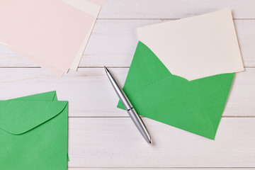 Top View of a invitation or Letter with a Green Envelope. Message or Ticket on Wooden White Desk or Table. Writing a note. Pen, Pencil, a Blank Notebook. Picture. Copy space for text or Image.