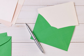 Top View of a invitation or Letter with a Green Envelope. Message or Ticket on Wooden White Desk or Table. Writing a note. Pen, Pencil, a Blank Notebook. Picture. Copy space for text or Image.