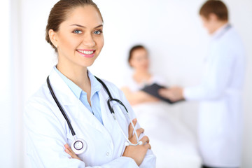 Cheerful smiling female doctor on the background with physician and his patient in the bed