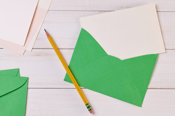 Top View of a invitation or Letter with a Green Envelope. Message or Ticket on Wooden White Desk or Table. Writing a note. Pen, Pencil, a Blank Notebook. Picture. Copy space for text or Image.