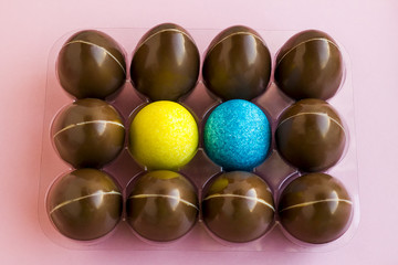 Decorative blue and yellow color Easter eggs in the holder with chocolate eggs.Pink surface,close up taken,isolated.