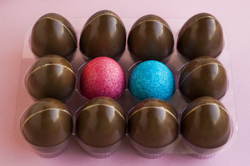 Decorative blue and pink color Easter eggs in transparent egg holder with chocolate eggs.Pink background,close up taken,isolated.