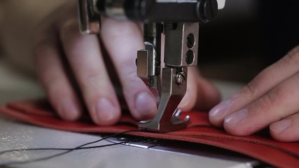 close up shot of the master hands, who uses a sewing machine to create stitches on a leather wallet, the needle slowly pierces the material
