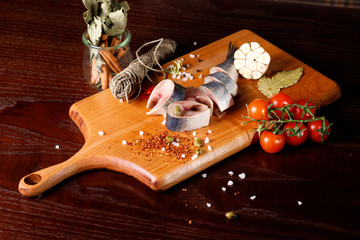 pieces of herring on a cutting Board, next to pepper and garlic and tomatoes on a branch.