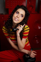 Studio fashion shooting.The girl in a bright outfit, top and pants flared in red and orange tones. Brunette with curly hair. Talking on the phone, chatting, flirting