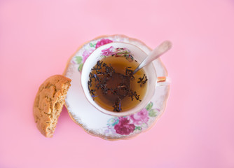 Loose leaf tea in an antique tea cup with a cookie on a pink backdrop