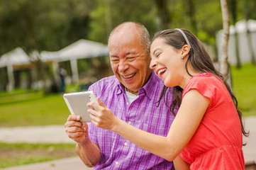 Outdoor view of father and daughter using a tablet looking somethings intefunny, in the park