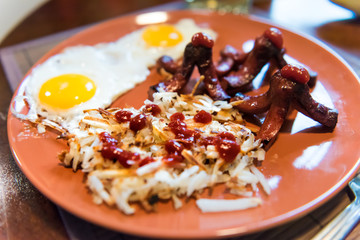 Closeup of large breakfast brunch plate with fried eggs, hash browns shredded potatoes, ketchup, sausage tako octopus