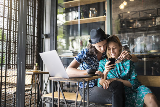 Artist couple sitting in cafe and checking the young woman's smartphone