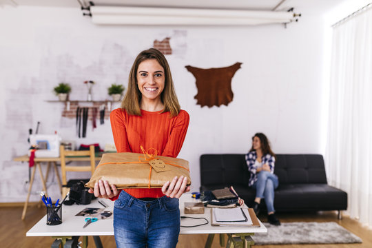 Smiling fashion designer holding a wrapped package in studio