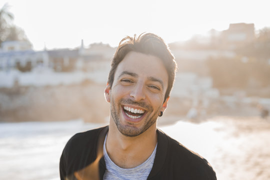 Portrait of laughing young man with stubble on the beach at sunset