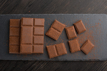 Milk chocolate with cocoa powder. Top view, on a wooden texture. C blank space for inscription or advertising.