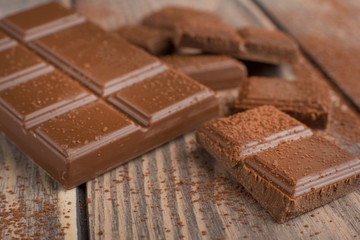 Milk chocolate with cocoa powder. On a wooden texture. Macro