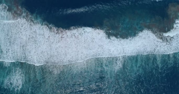 Aerial pull back showing waves breaking with swirling undertow underneath