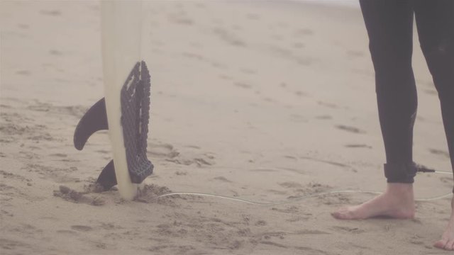 Close up shot of a surfer sticking his surf board in the sand