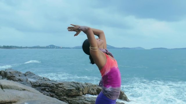 Woman practicing yoga asanas salutation to sun Surya Namaskar on ocean coast