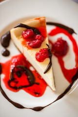 Slice of New York Cheesecake with Raspberries, Berry Sauce and Chocolate Swirled on a White Plate