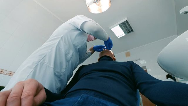 Man is sitting in an armchair at the dentist. Female doctor conducts the procedure. Low wide angle shot