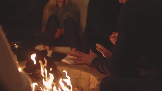 Focusing close up shot of some young people relaxing by a patio fire at night
