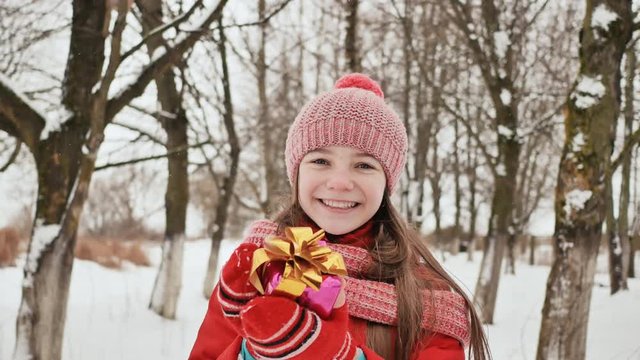 A beautiful young schoolgirl standing in a snowy forest in the winter takes a joyful gift from the hands of a friend.